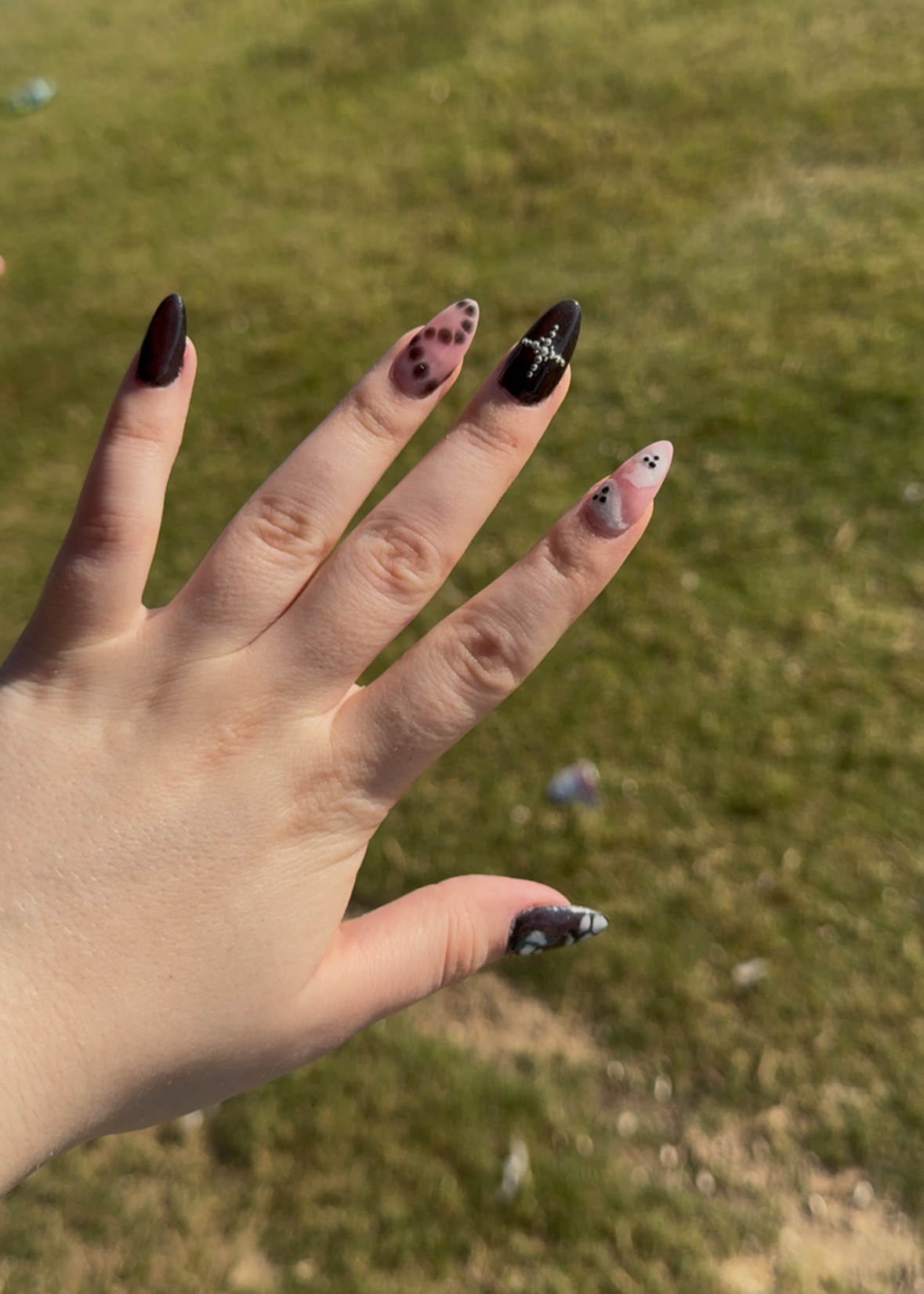 Hand with black nail polish against a grassy background